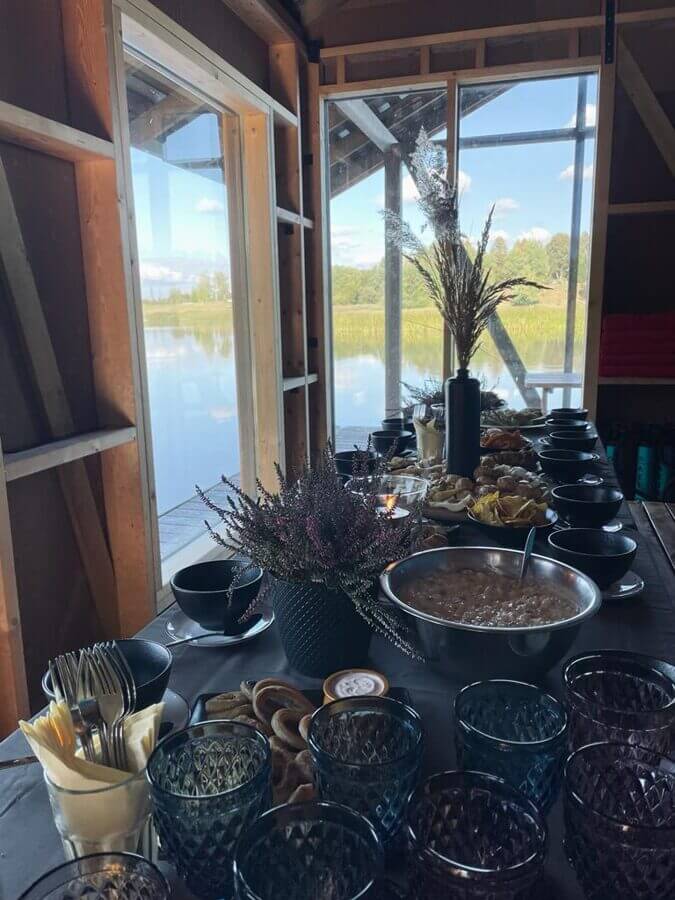 Uzkodu galds ar traukiem un ēdieniem Murdiņu  koka Pontonā ar skatu uz upi.