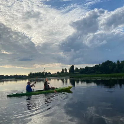 Divi cilvēki airē zaļā kajakā Daugavā.