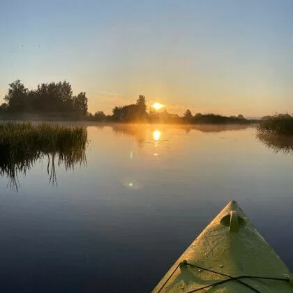 Saullēkts un zaļš kajaks mierīgajā Daugavā.