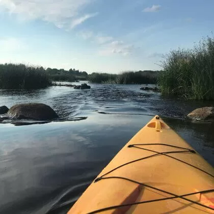 Dzeltens kajaks upē ar zālēm un akmeņiem.